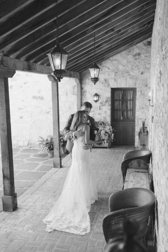 Black and white photo of the bride and groom embracing in a stone hallway at Holman Ranch.
