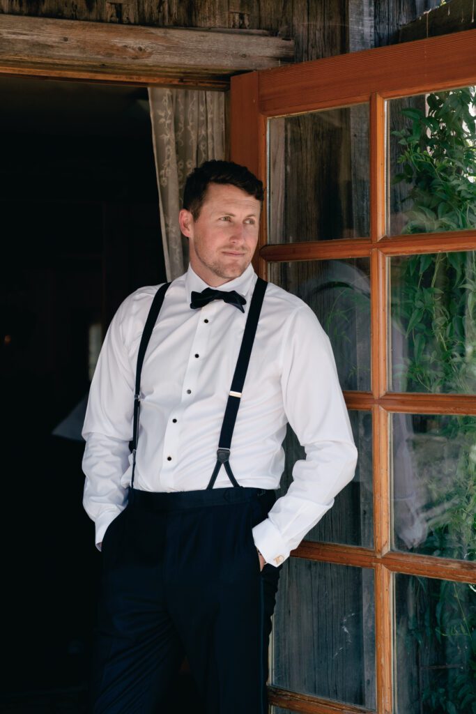 Groom in classic black tuxedo standing outside rustic barn at Olympias Valley Estate wedding in Petaluma, California