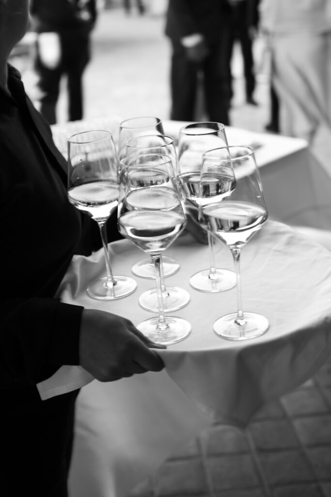 Black and white photo of champagne glasses being served during wedding reception
