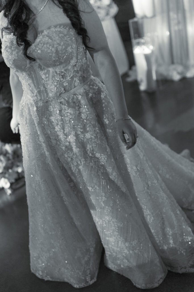 Black and white detail of bride wearing beaded wedding gown during reception
